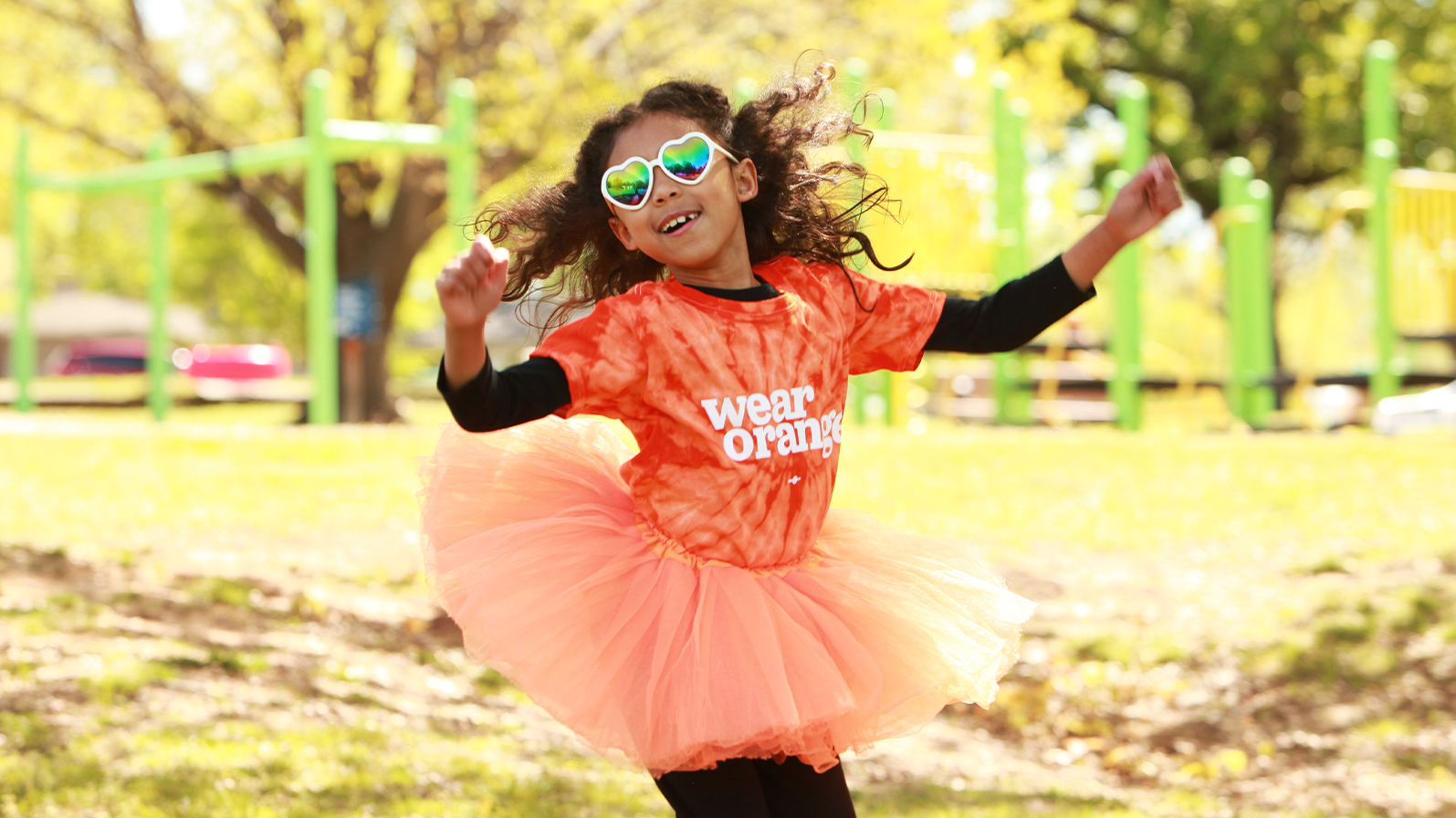 A young girl jumping while wearing a Wear Orange tie-dye shirt